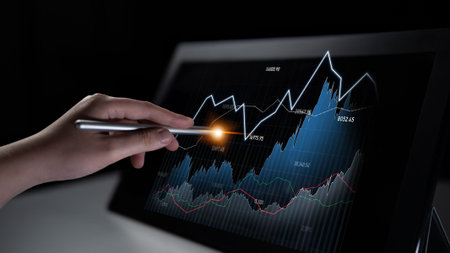 A hand uses a stylus on a digital tablet displaying a financial chart that emphasizes stock market...