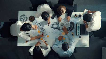 Top view of engineer pointing at turbine engine at meeting table with equipment. Aerial view of...