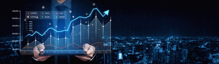 A businessman stands against a stunning city skyline at night, holding a tablet displaying financial data, growth trends, and market performance metrics.の写真素材