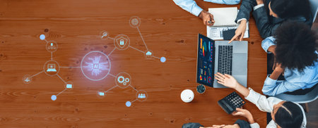 Group of professionals engaging in a collaborative meeting over a wooden table, utilizing laptops...