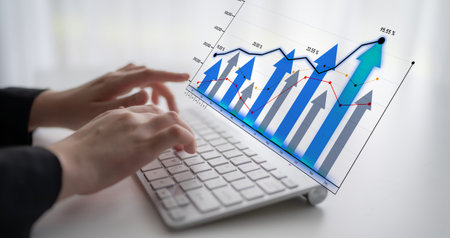 A focused workspace scene featuring hands typing on a laptop with dynamic graphs and charts...