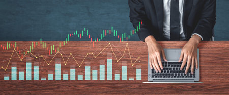 A business professional analyzes financial market data while typing on a laptop. Graphs and charts...