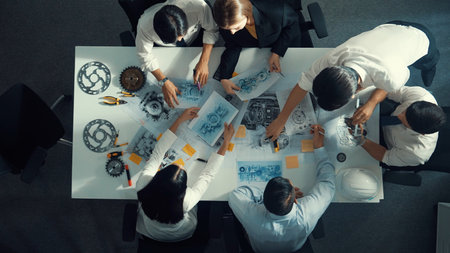 Top view of engineer pointing at turbine engine at meeting table with equipment. Aerial view of...