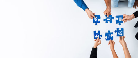 Overhead view of diverse hands assembling blue puzzle pieces symbolizing business concepts such as...