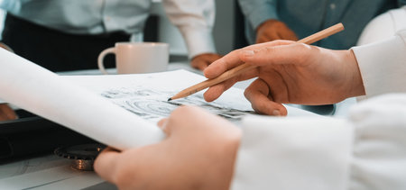 Close-up view of hands actively engaged in sketching architectural designs with a pencil. A...