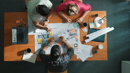 Top down view of civil engineers using tablet to design house structure while sitting at table with project plan placed. Aerial view of team planning and sharing idea about construction. Symposium.の写真素材