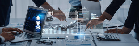 A group of professionals engage in collaborative data analysis using laptops and charts in a modern...