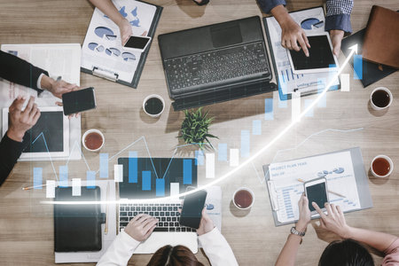 A dynamic business team collaborates in a meeting, analyzing financial data on laptops and...