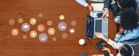 A diverse business team collaborates at a wooden table, engaging with a laptop and documents while...