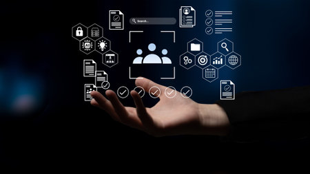 A hand holds a futuristic digital interface featuring various icons related to data management,...