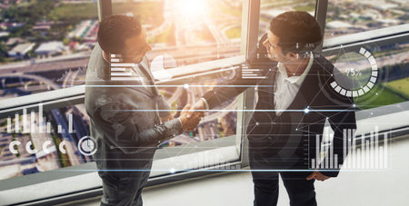 Two business professionals shake hands in a high-rise office, showcasing collaboration and...