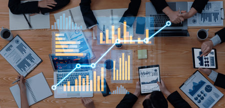 A dynamic business meeting featuring professionals analyzing financial reports with laptops and...