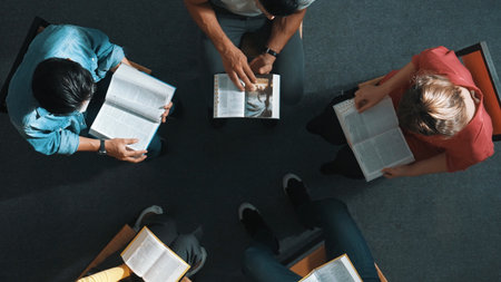 Top down view of people reading a book and sitting in circle with book on laps. Aerial view of diverse people looking at book while studying with faith, trust and hope, calm. Symposium.の写真素材