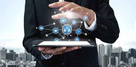 A businessman interacts with a tablet displaying digital network connections against a city skyline,...