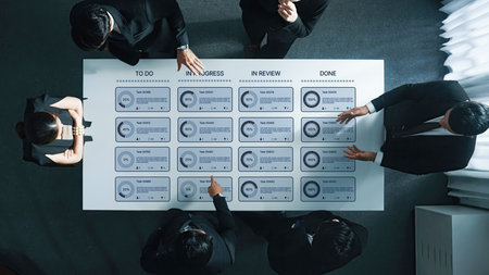 A group of business professionals engages in a strategic meeting, analyzing project statuses on a...