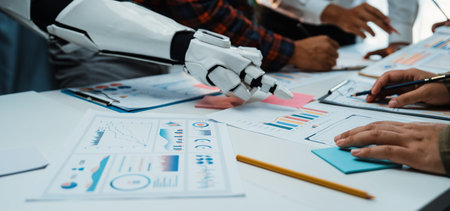A futuristic office scene showcasing collaboration between humans and a robot. The focus is on analyzing charts and data for effective decision-making and innovative solutions.の写真素材