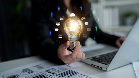 Business professional holding glowing light bulb with digital icons representing innovation, technology, and data analytics in a modern workspace.の写真素材