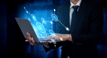 A business professional stands in a modern office environment, using a laptop that displays a...