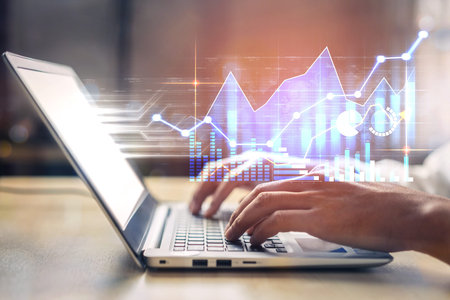 A close-up view of a person typing on a laptop, showcasing financial data and graphs in an office...