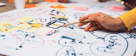 A close-up view of hands involved in brainstorming with sticky notes on chart paper, showcasing teamwork, creativity, and idea generation in a collaborative workspace.の写真素材