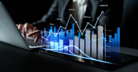 A business professional engages with a laptop, analyzing digital graphs and statistics. This scene...