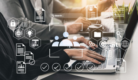 A person uses a laptop in a modern workspace, surrounded by digital icons representing business,...