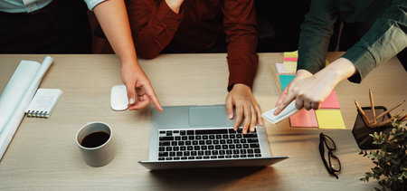 A group of professionals collaborates in a modern office setting, focusing on a laptop while sharing...