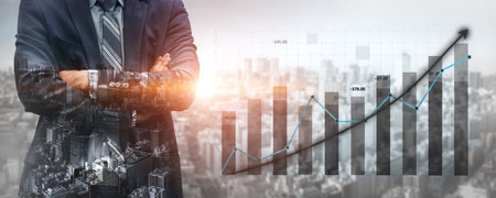 A businessman stands confidently in front of a city skyline while visualizing financial growth through graphs, highlighting strategic success in business.の写真素材