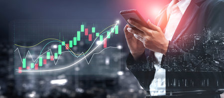 A businessman engages with his smartphone while analyzing stock market trends through dynamic...
