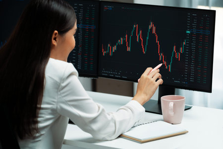 Young beautiful Asian businesswoman looking on pc to analyze profitable of exchange stock market...