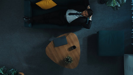 Top down aerial view of smart businessman working on laptop while lying on sofa to relieve stress....