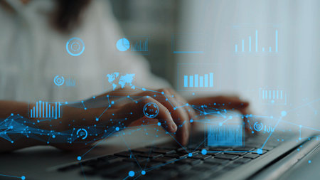 Close-up view of hands typing on a laptop with digital overlays of graphs and charts, representing...