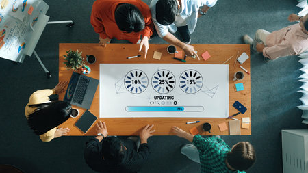 Professionals collaborate in an office setting, engaging over visuals of progress updates displayed...