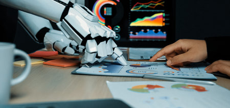 A robotic arm interacts with a human hand over data charts, signifying the blend of technology and...