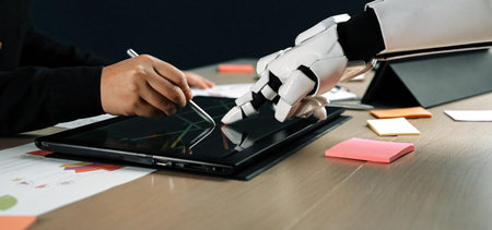 A robot hand and human hand illustrate collaboration in technology as they interact with a tablet,...