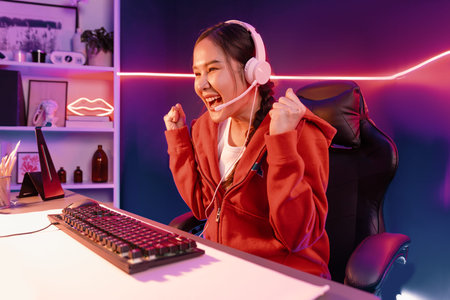 Host channel of smiling beautiful Asian girl streamer playing with raising fist up winning on Esport skilled team players wearing headphones pastel color, fighting online game at neon room. Stratagem.の写真素材