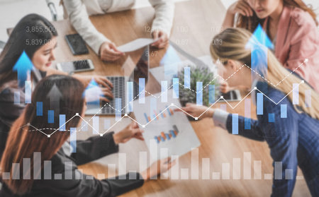 A diverse group of professionals gathers around a table to discuss financial strategies, analyzing charts and data in a productive and modern office environment.の写真素材