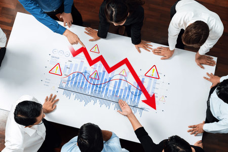 A business team gathered around a table analyzing a declining graph with warning signs. The scene...