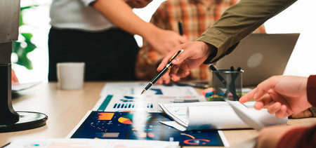 A business team collaborates in an office environment, analyzing charts and documents on a table....