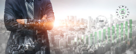 A confident businessman stands in front of a city landscape, symbolizing growth and sustainability, with future targets for green initiatives represented in visual graphs. Gantryの写真素材