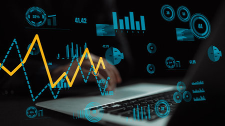 A professional workspace scene featuring a laptop with vibrant data visualizations showing graphs,...