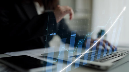 A professional business person reviews financial data on a laptop, with an overlay of growth trends,...
