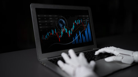 A robotic hand engaged with a laptop showing dynamic financial graphs and analytics. This image...