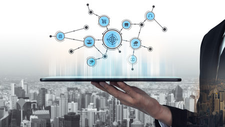 A hand holds a tablet displaying a digital network interface with various icons representing...