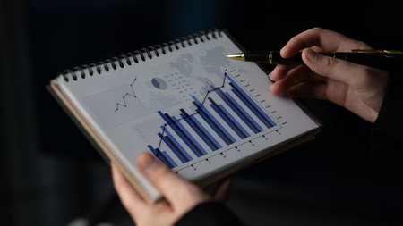 A person is holding a notepad filled with graphs and charts showcasing financial data and market...