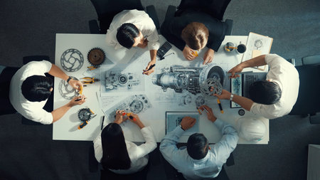 Top view of engineer pointing at turbine engine at meeting table with equipment. Aerial view of...