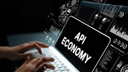 Hands Typing on Laptop with API Economy Concept and Digital Data Visualizations in a Dark...