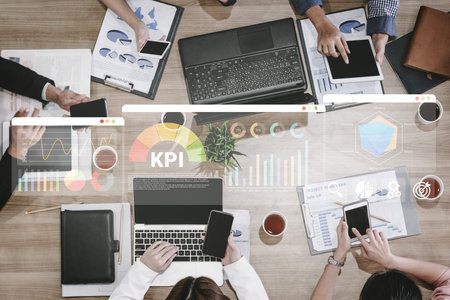 Professionals engage in a business meeting, utilizing laptops and smartphones to analyze metrics and data, fostering collaboration and strategic planning in an office environment. Ledger