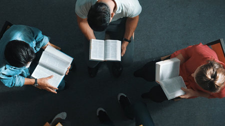 Top down view of prayer reading at bible book and sitting in circle with bible book on laps. Aerial view of diverse people looking at book while studying with faith, trust and hope, calm. Symposium.