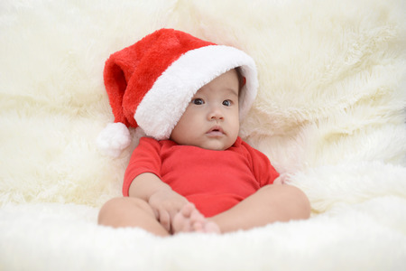 asian cute baby sitting on a soft cloth in the living room. Baby with Santa hatの写真素材